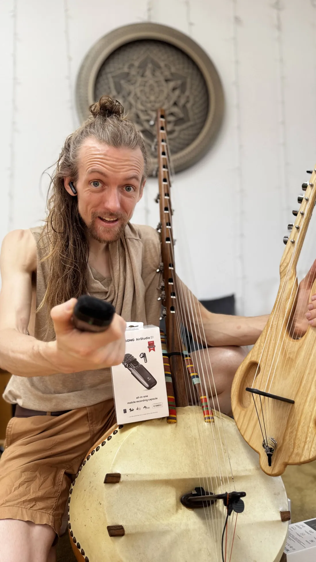 David Lesage tient le Gonilélé, la harpe africaine à calebasse, et montre le micro Hisong AirStudio S1 qui sert à la sonoriser.