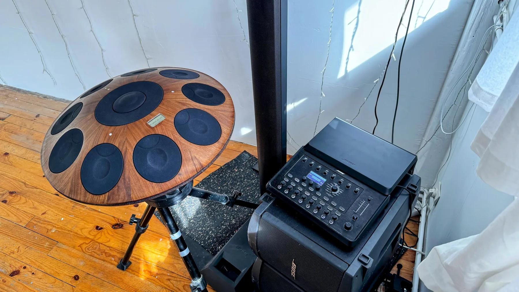 Un handpan électronique Neotone en bois posé sur son trépied, à côté de la sonorisation du showroom : une colonne Bose L1 Model II et sa console de mixage T8S posée sur les caissons.