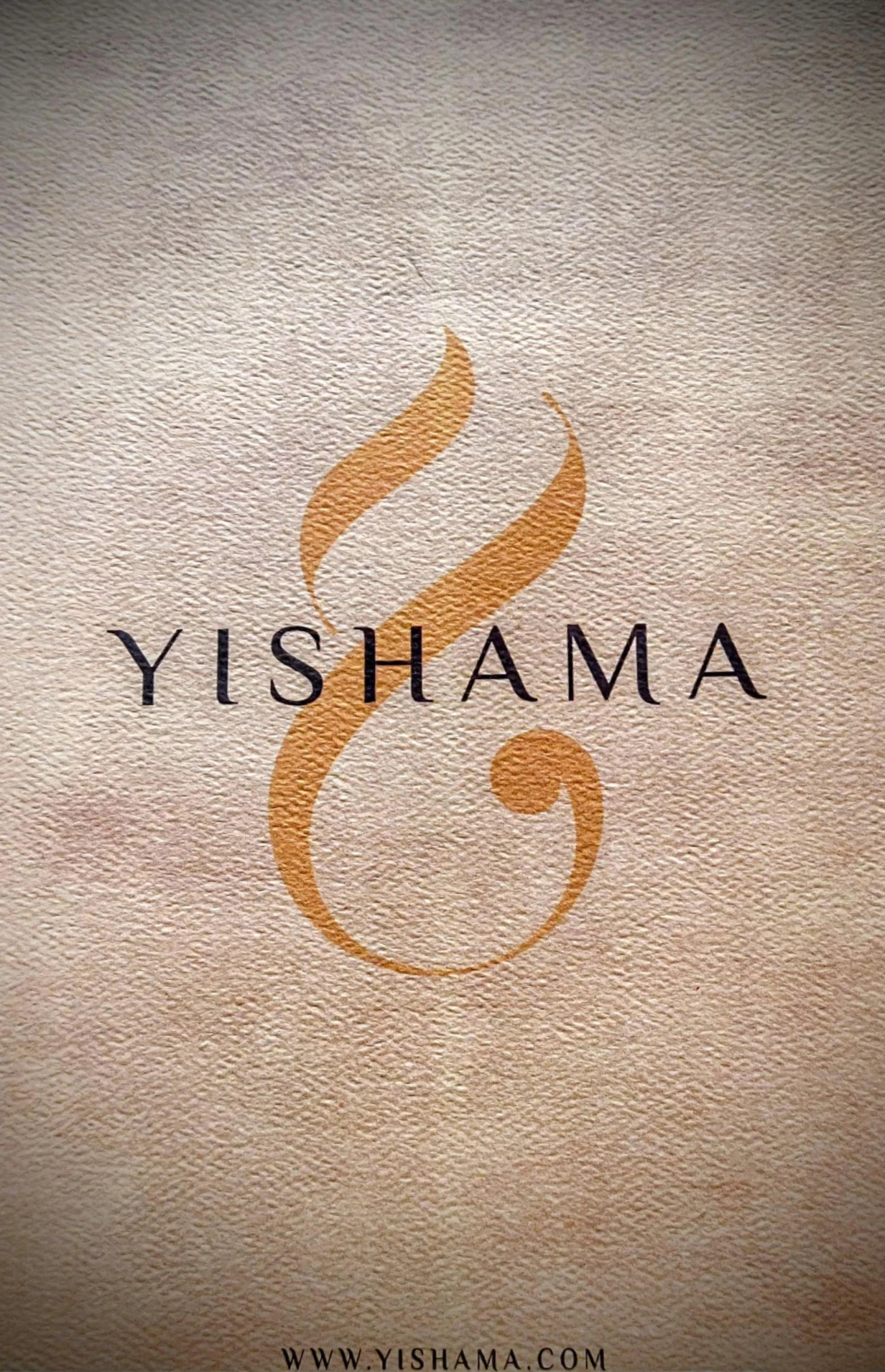 Le dos du certificat : le logo Yishama — une volute dorée — au-dessus du mot YISHAMA en capitales, sur papier texturé, avec l’adresse WWW.YISHAMA.COM en bas de page.